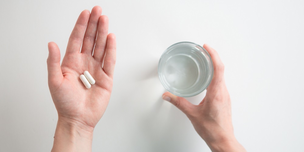 Mani che tengono due capsule e un bicchiere d'acqua.