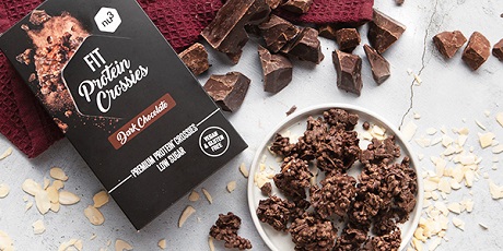 Prodotto e ingredienti su un tavolo. « FIT Protein Crossies » e pezzi di cioccolato.